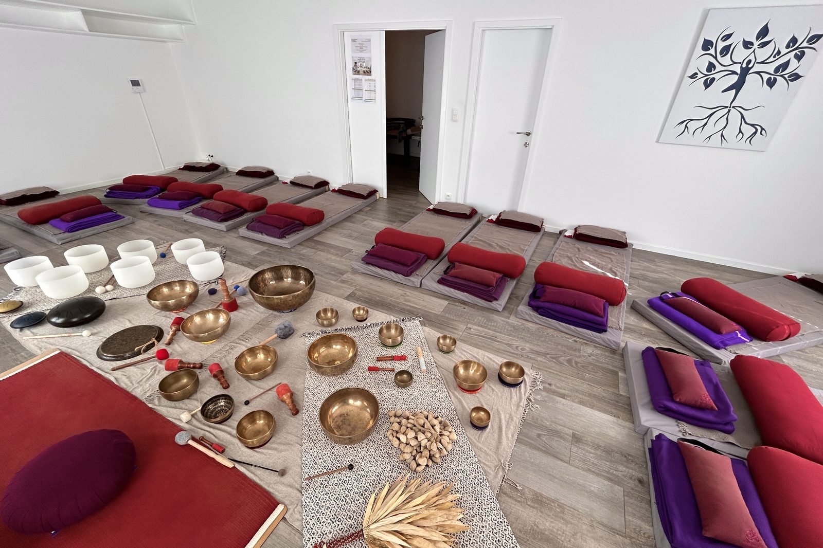La salle installée pour un voyage sonore : tapis, bolsters et couvertures, les bols et le gong au sol, l’arbre d’Aroma au mur