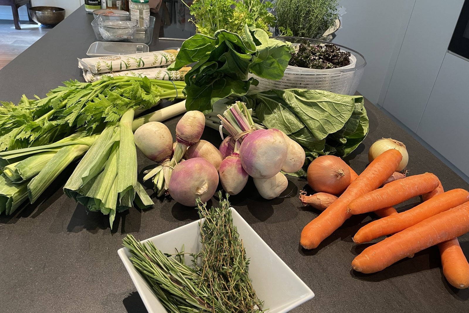 Des légumes frais sur un plan de travail : navets, carottes, oignons, céleri et un bol de thym