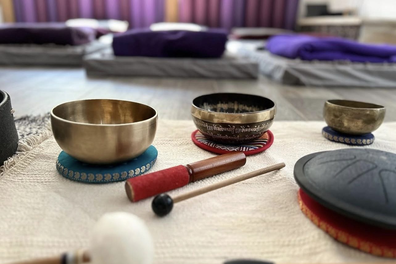 Trois bols chantants et leurs maillets posés sur un tissu clair, les tapis flous à l’arrière-plan